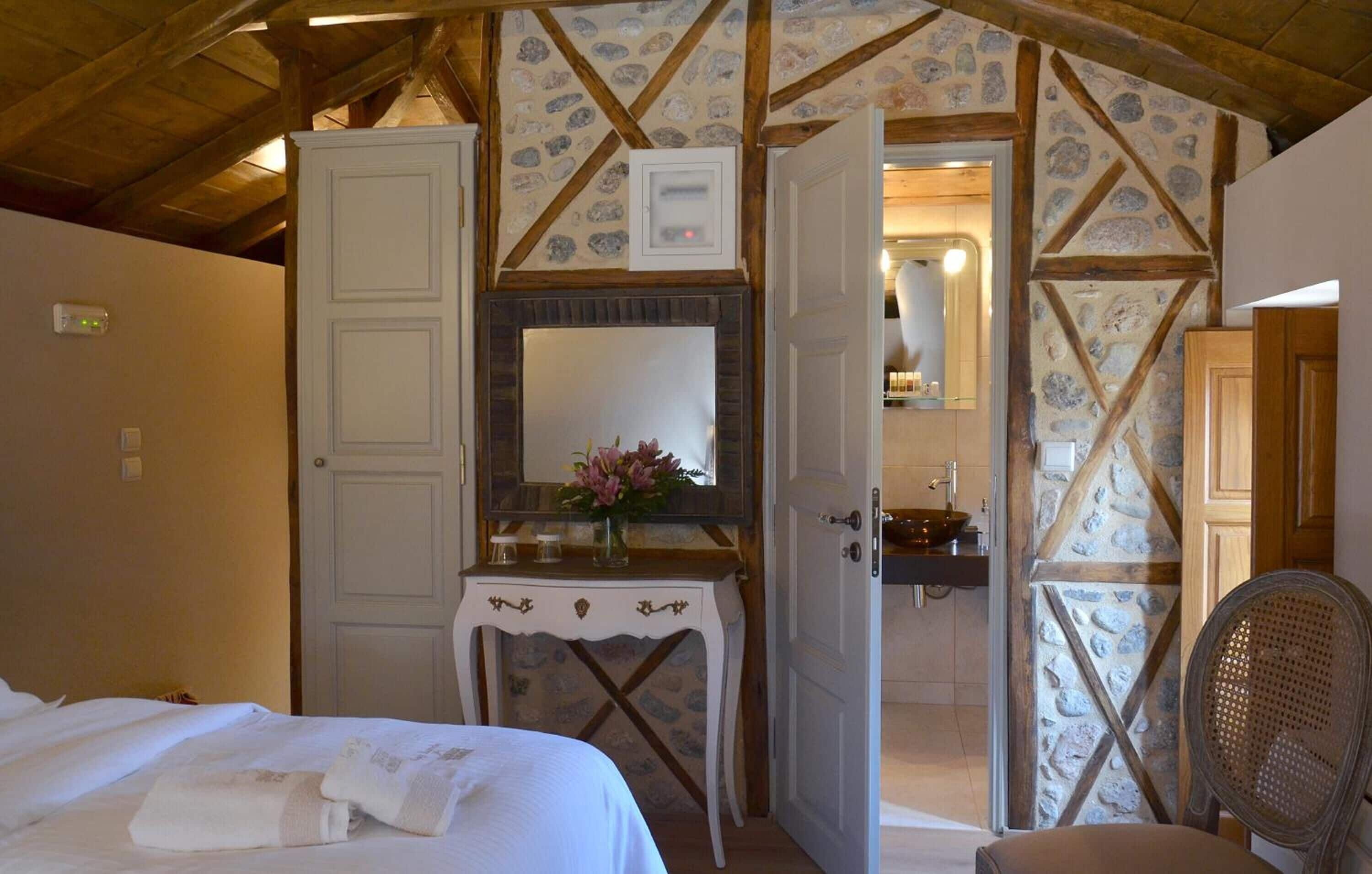 A bedroom with a bed, a bedside table with a vase, a mirror, and a wooden wall with a stone pattern.