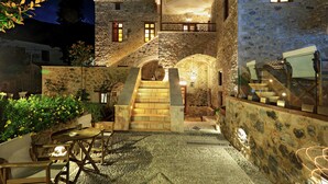 A stone building with a staircase leading to a balcony, outdoor seating area, and a well-lit entrance. - Archontiko Chioti (South Kynouria)