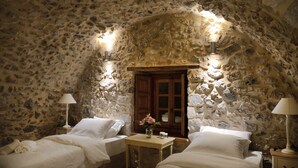 A stone-walled bedroom with two beds, a wooden door, and a small table with a vase of flowers. - Archontiko Chioti (South Kynouria)