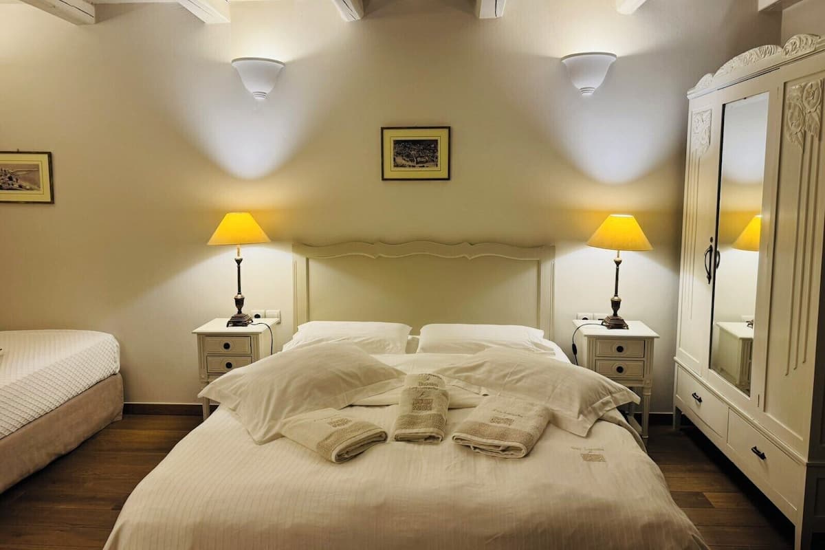 Hotellihuone, jossa on suuri sänky, kaksi yöpöytää valaisimineen, vaatekaappi ja seinällä oleva kehystetty taulu.