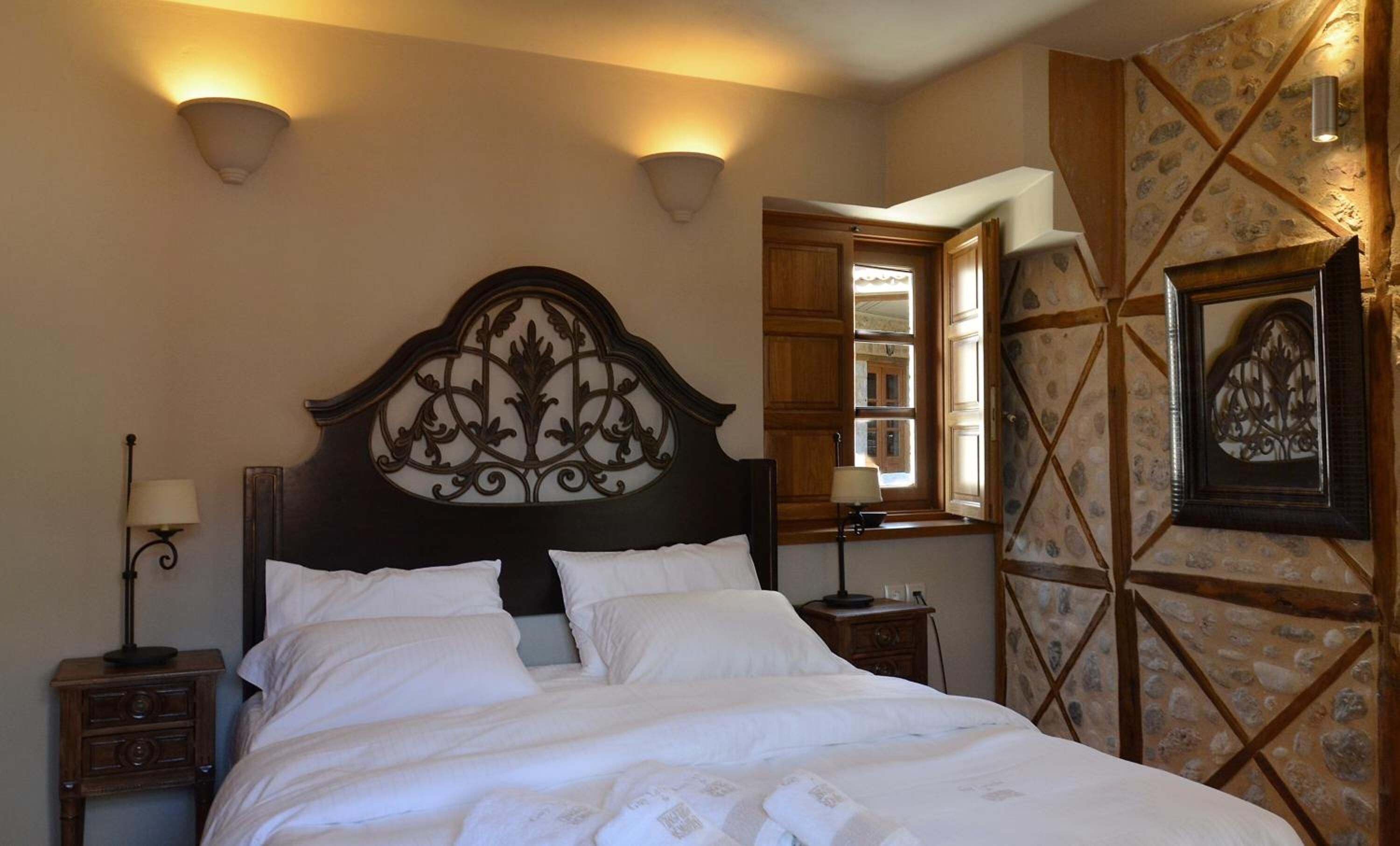 Uma cama bem arrumada com cabeceira decorativa, mesa de cabeceira com abajur e parede com padrão de pedra e uma obra de arte emoldurada.