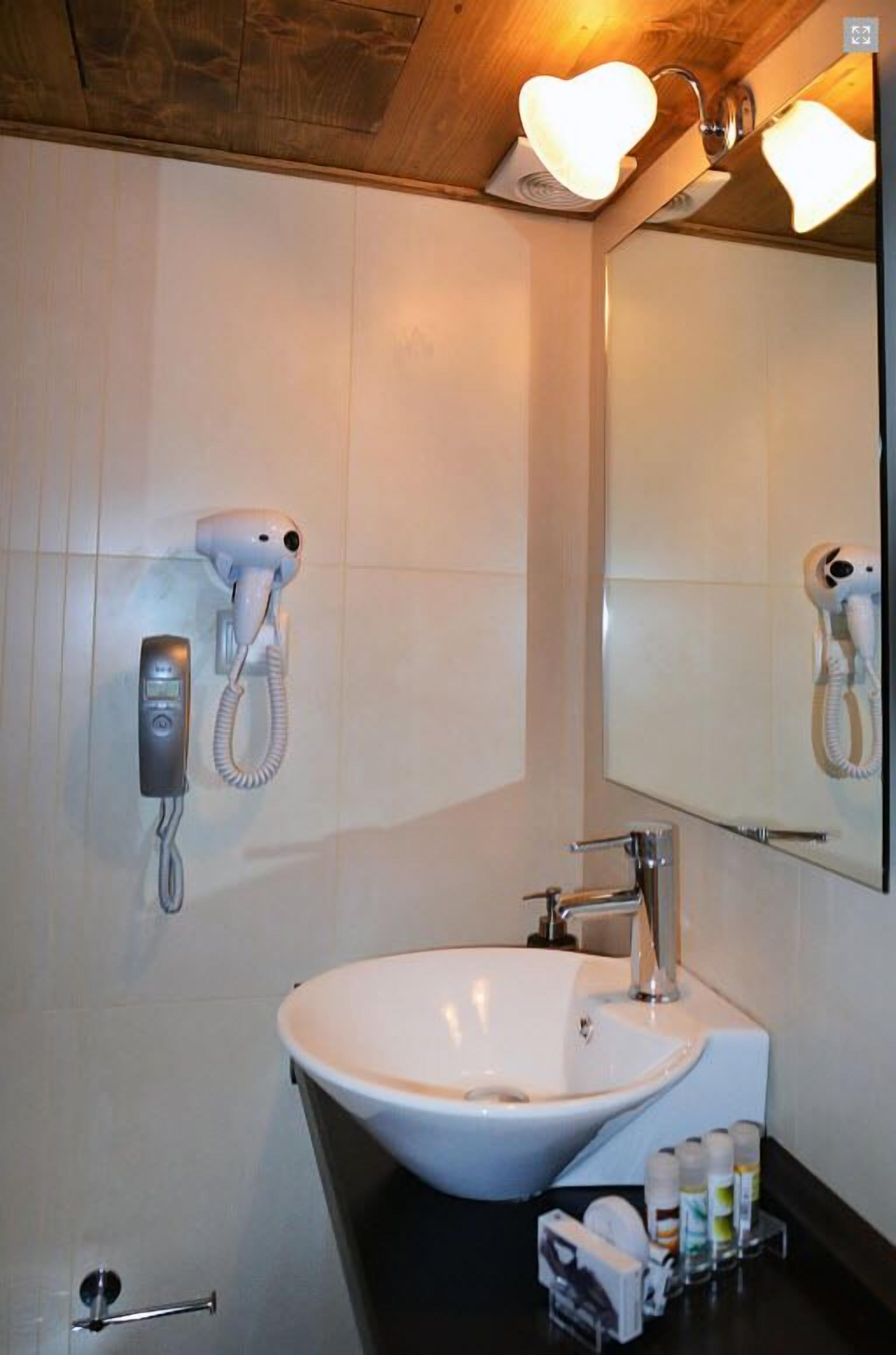 Un baño con un lavamanos blanco, un secador de pelo y un teléfono.