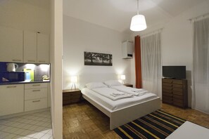A hotel room with a bed, bedside lamps, a flat-screen TV, a painting on the wall, and a kitchen area with cabinets and a microwave. - Heart of Vienna Harmoniegasse (Vienna)