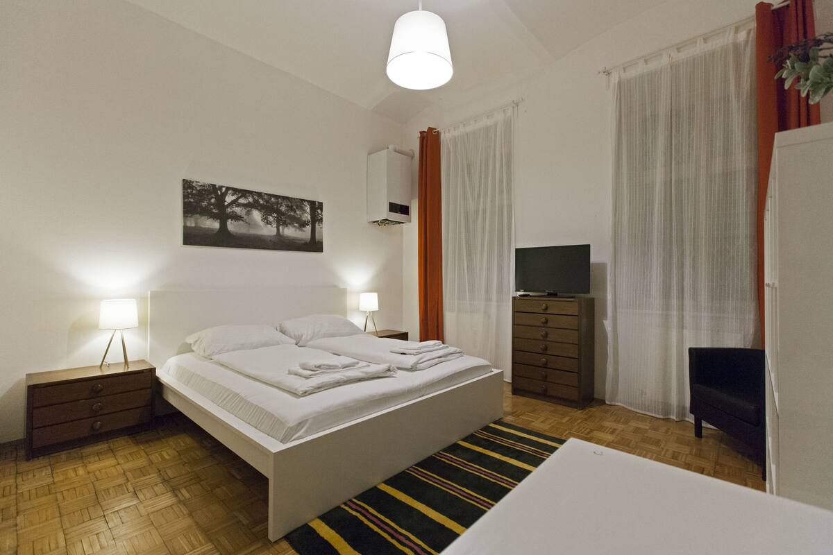 A neatly arranged bedroom with a bed, bedside lamps, a television, and a dresser.