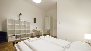 A hotel room with two beds, a desk, a chair, a wardrobe, and a shelf unit. - Heart of Vienna Harmoniegasse (Vienna)