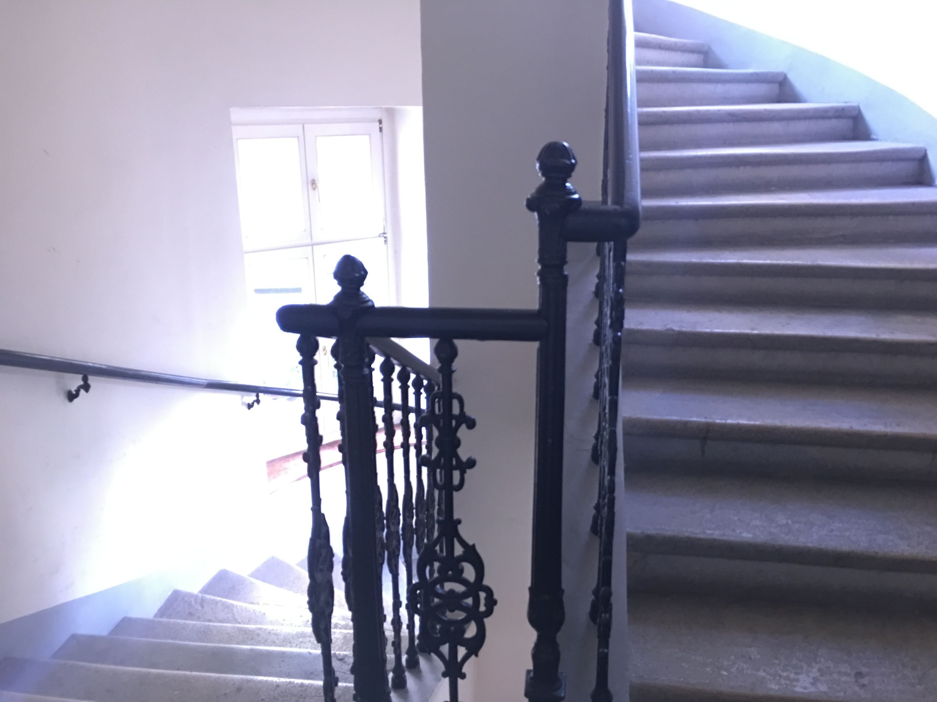 Uma escadaria com balaústres pretos decorados e uma parede branca.