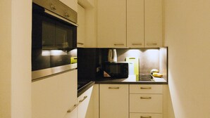 A compact kitchen with white cabinets, a black microwave, and a small countertop. - Heart of Vienna Harmoniegasse (Vienna)
