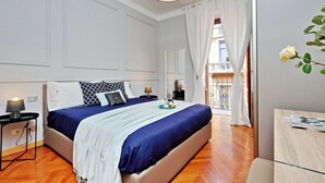 A bedroom with a large bed, bedside lamps, a small table, and a view of the balcony. - JOIVY Austere Elegance (Milan)