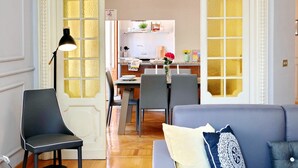 A modern living room with a grey sofa, a black chair, and a dining area with a table and chairs. - JOIVY Austere Elegance (Milan)