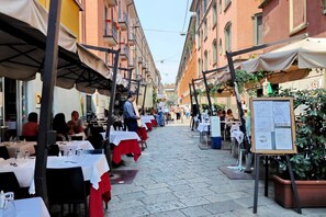An outdoor dining area with tables set up along a cobblestone street, surrounded by buildings with balconies. - JOIVY Austere Elegance (Milan)