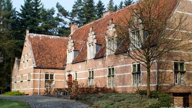 A traditional brick building with a tiled roof, multiple chimneys, and a cobblestone pathway leading to a bench. - Hotel Keravic (Kasterlee)