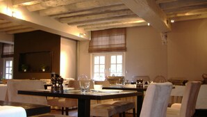 A dining area with a long table, multiple chairs, and a window with blinds. - Hotel Keravic (Kasterlee)