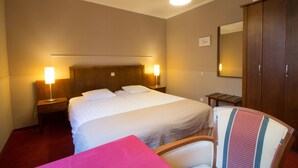 A hotel room with a large bed, two bedside lamps, a wooden wardrobe, and a chair with a striped cushion. - Hotel Keravic (Kasterlee)
