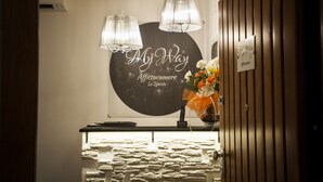 A reception area with a stone wall, two pendant lights, a floral arrangement, and a sign that reads "My Way Affittacamere La Spezia." - My Way (La Spezia)