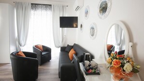 A modern living room with a sofa, two armchairs, a flat-screen TV, a coffee table with a vase of flowers, and a large mirror. - My Way (La Spezia)