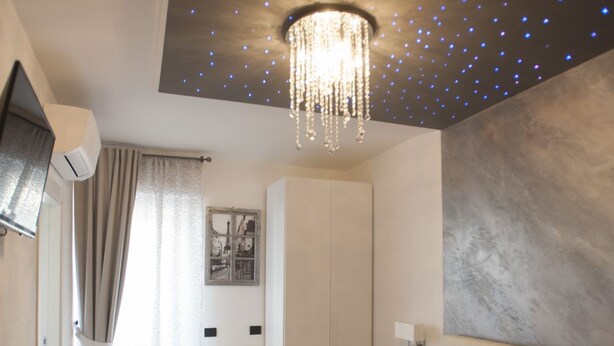 A modern bedroom with a large bed, a chandelier, a wardrobe, and a painting on the wall. - My Way (La Spezia)