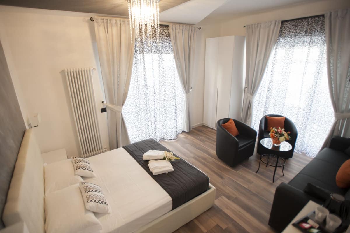 Ein modernes Hotelzimmer mit einem Bett, einer Sitzecke mit Tisch und großen, mit Vorhängen versehenen Fenstern.