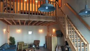 Un loft spacieux avec un plafond haut, des poutres apparentes, un escalier avec une rampe en bois et un coin salon confortable comprenant un canapé, des fauteuils et une petite table.