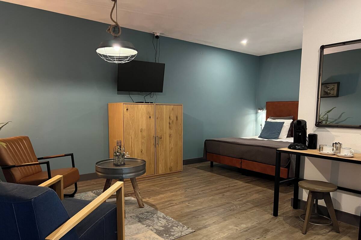 A compact hotel room with a bed, a desk, a chair, a wardrobe, and a television.