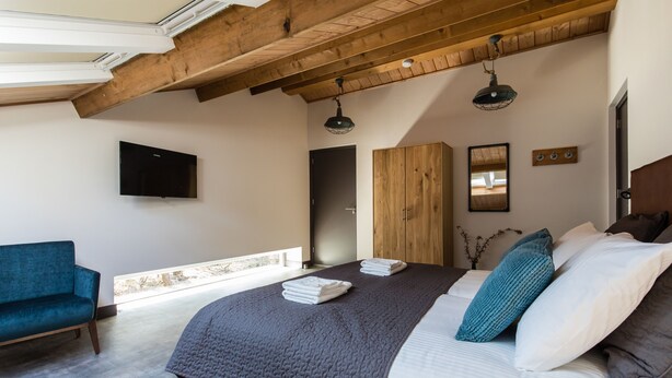 Une chambre avec un grand lit, une armoire en bois, un canapé bleu et un téléviseur fixé au mur.