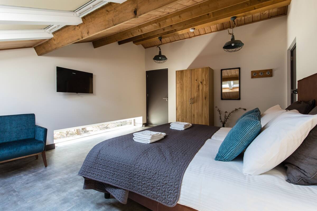 A bedroom with a large bed, a wooden wardrobe, a blue sofa, and a television on the wall.