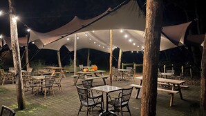 Un espace de restauration en plein air, avec des tables et des chaises disposées sous de grandes tentes, illuminé par des guirlandes lumineuses.