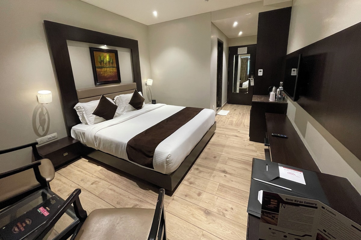 A hotel room with a large bed, a desk with a computer, a TV, and a mirror.