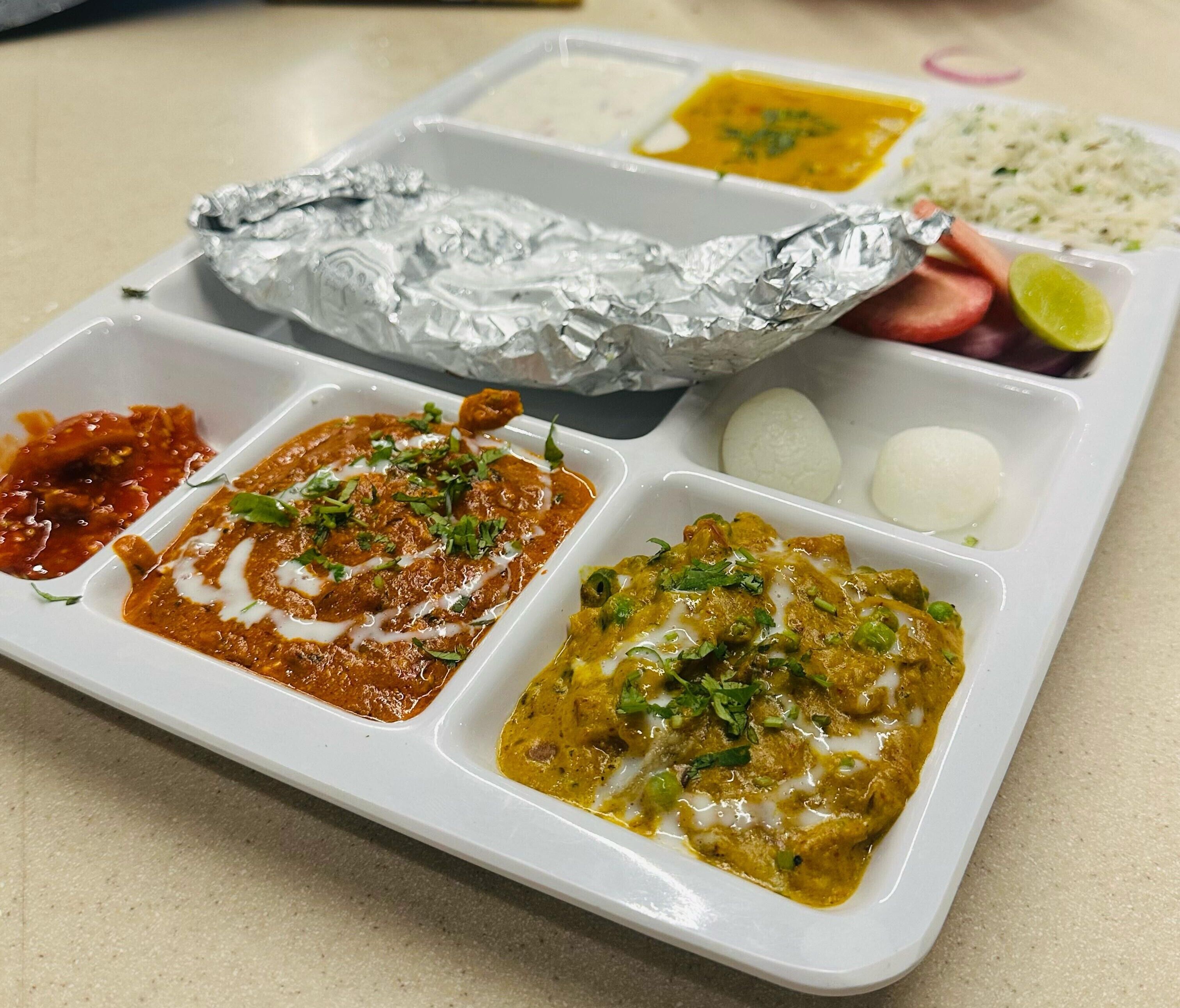 A meal tray with various dishes including curry, rice, and a side of vegetables.