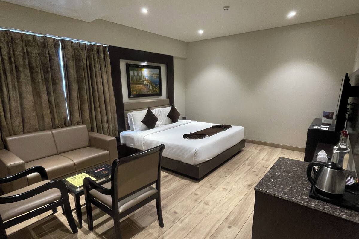 A modern hotel room with a bed, a sofa, a small table, and a coffee machine.