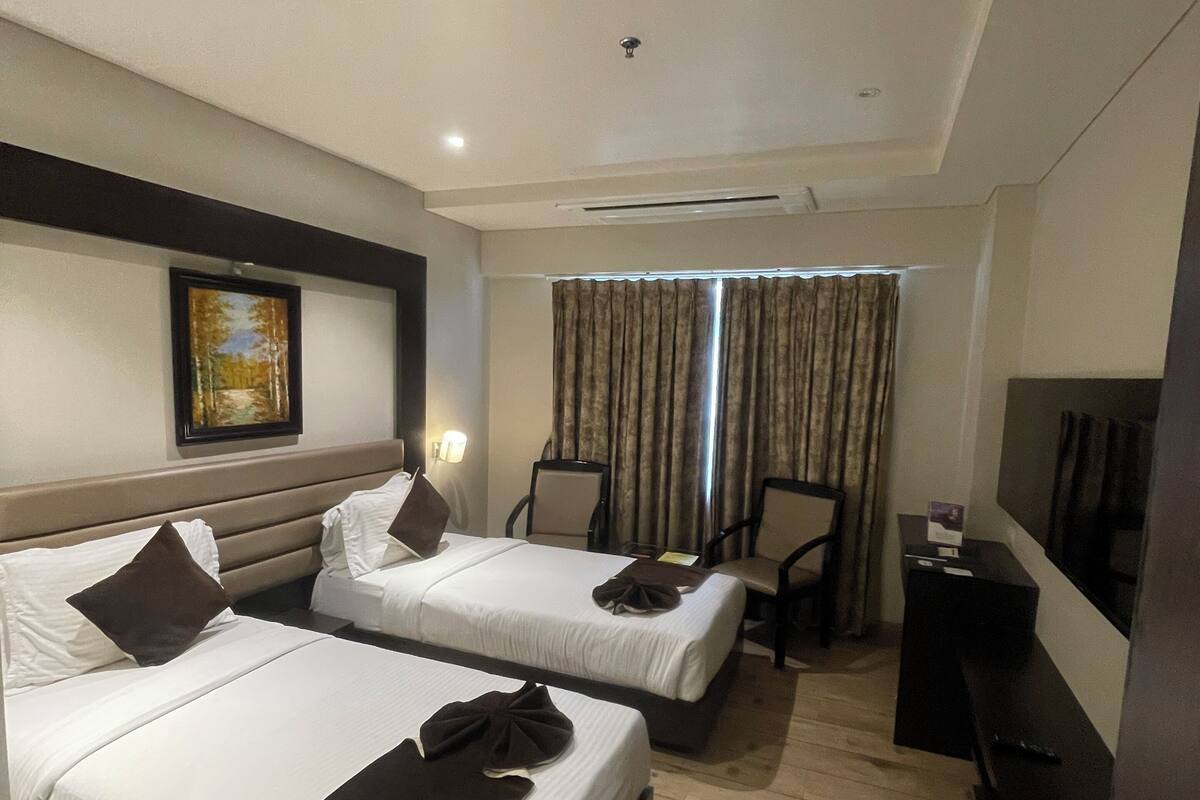 A hotel room with two beds, a desk, a chair, a TV, and a painting on the wall.