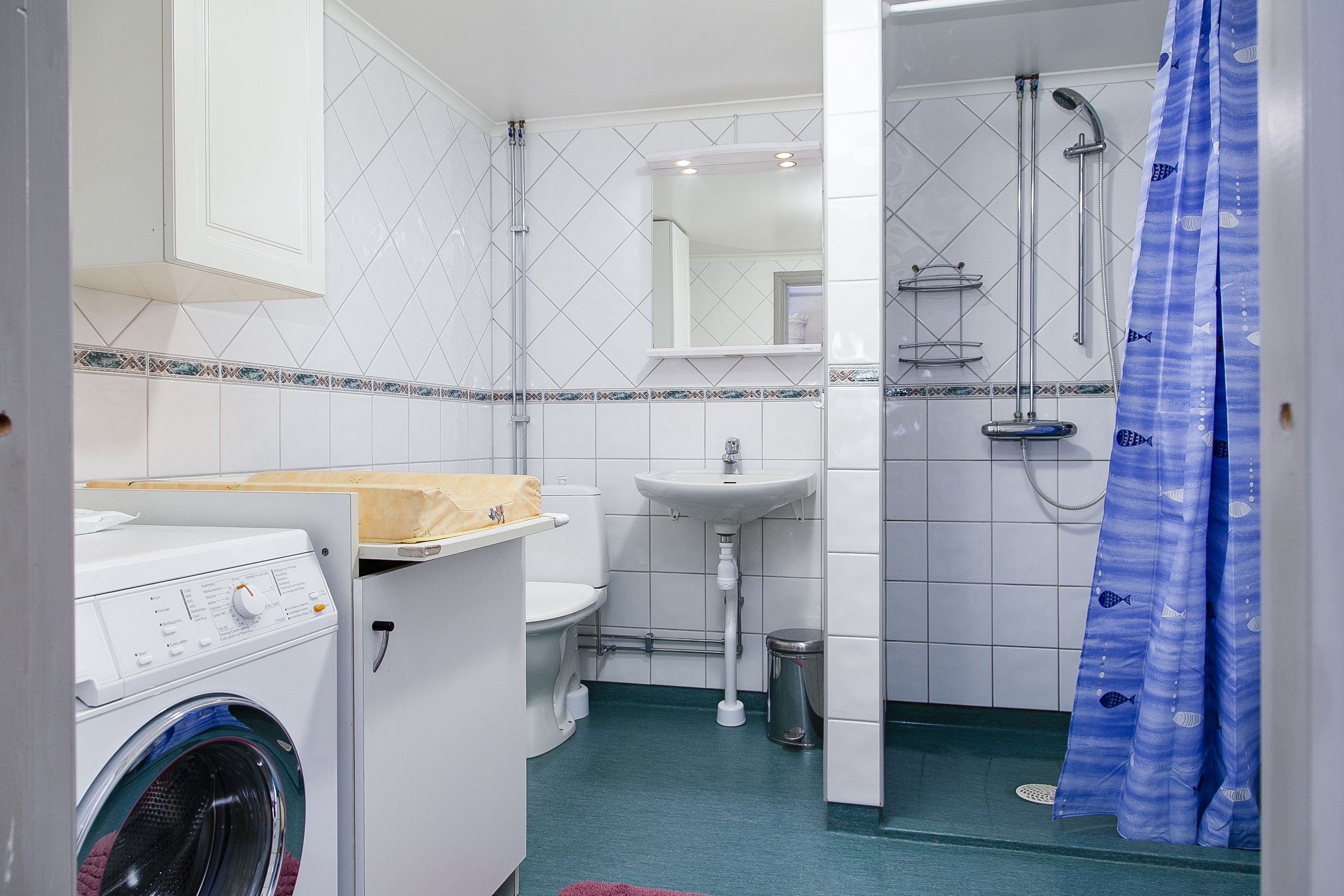 A compact bathroom with a washing machine, sink, and shower.