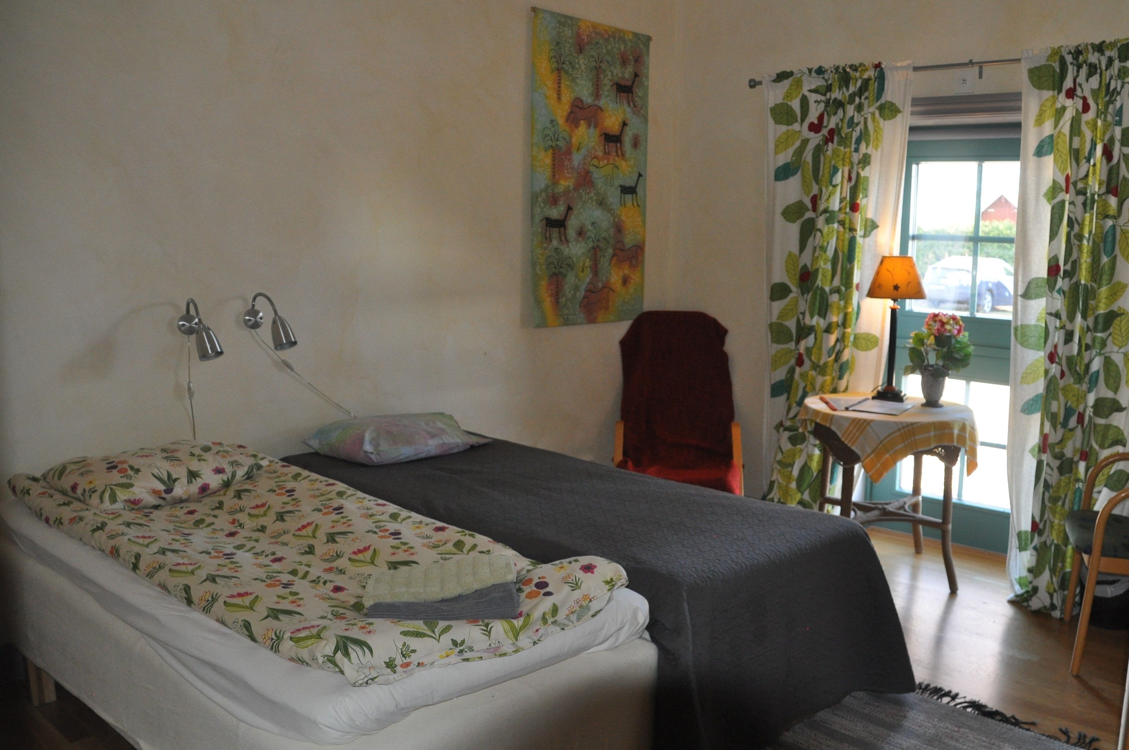 Quarto com cama, poltrona, mesa com luminária e cortinas.