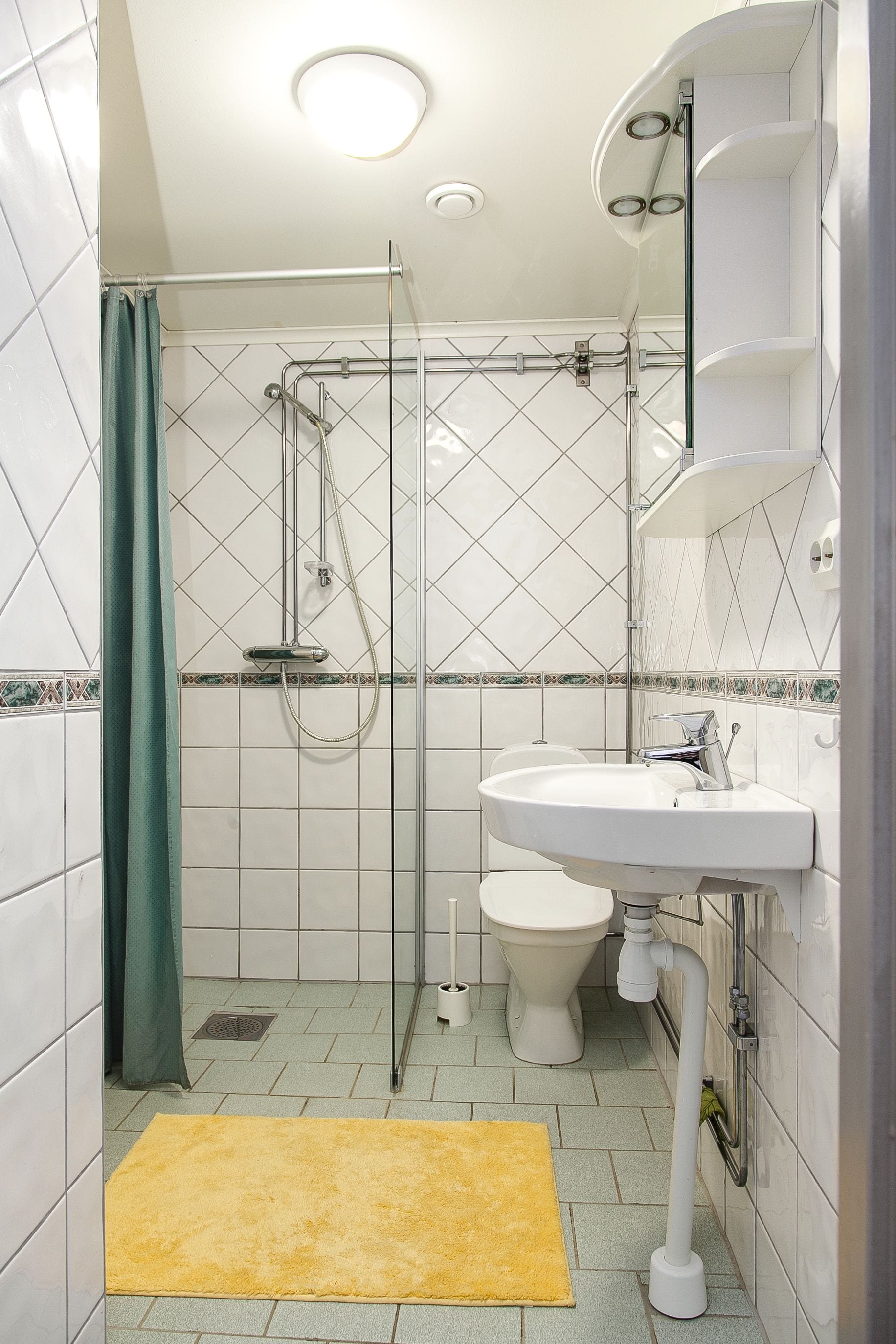 A bathroom with a shower, toilet, sink, and a yellow rug.