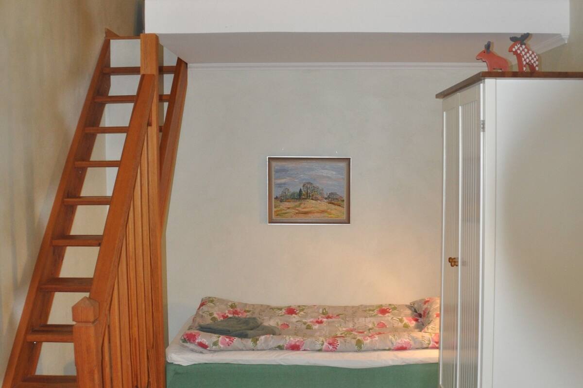 A room with a bunk bed, a wooden ladder, a green sofa, a framed landscape painting, and a white wardrobe.