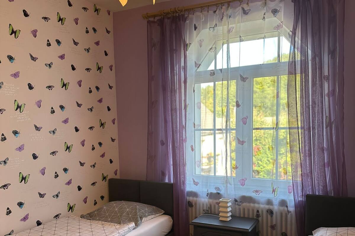 A bedroom with two beds, a bedside table, a lamp, and a window with curtains.