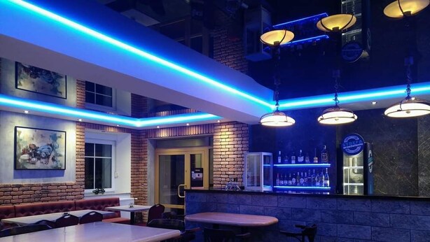 A restaurant with brick walls, blue neon lighting, and hanging pendant lights. Tables and chairs are arranged for dining. - Dom go ścinny Gerus (Lubomierz)