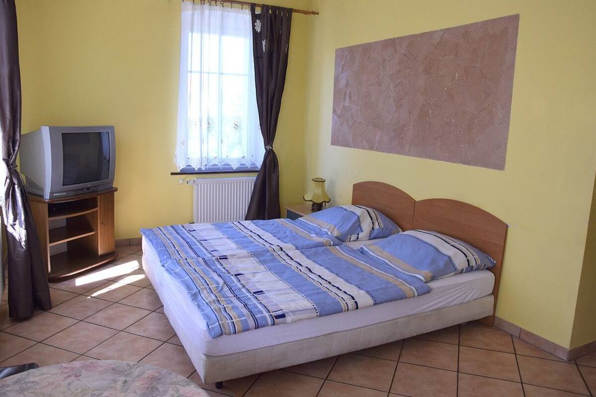 A bedroom with a bed, a television on a wooden stand, a window with curtains, and a wall with a textured pattern.