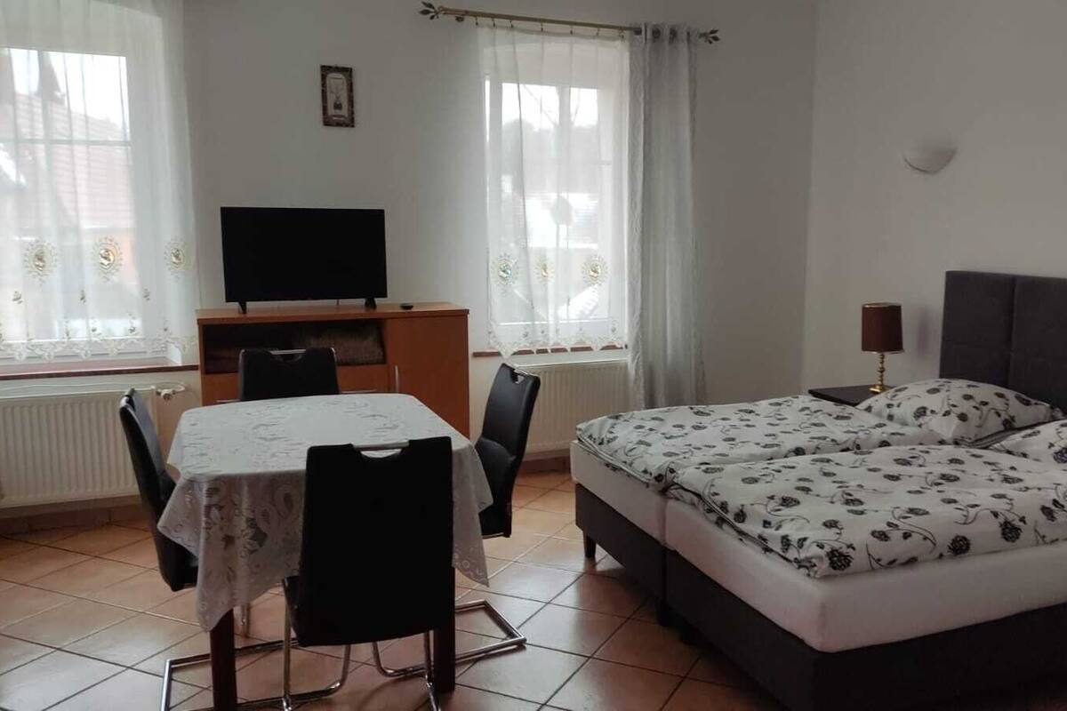 A bedroom with a bed, a desk, a chair, a table, and a TV.