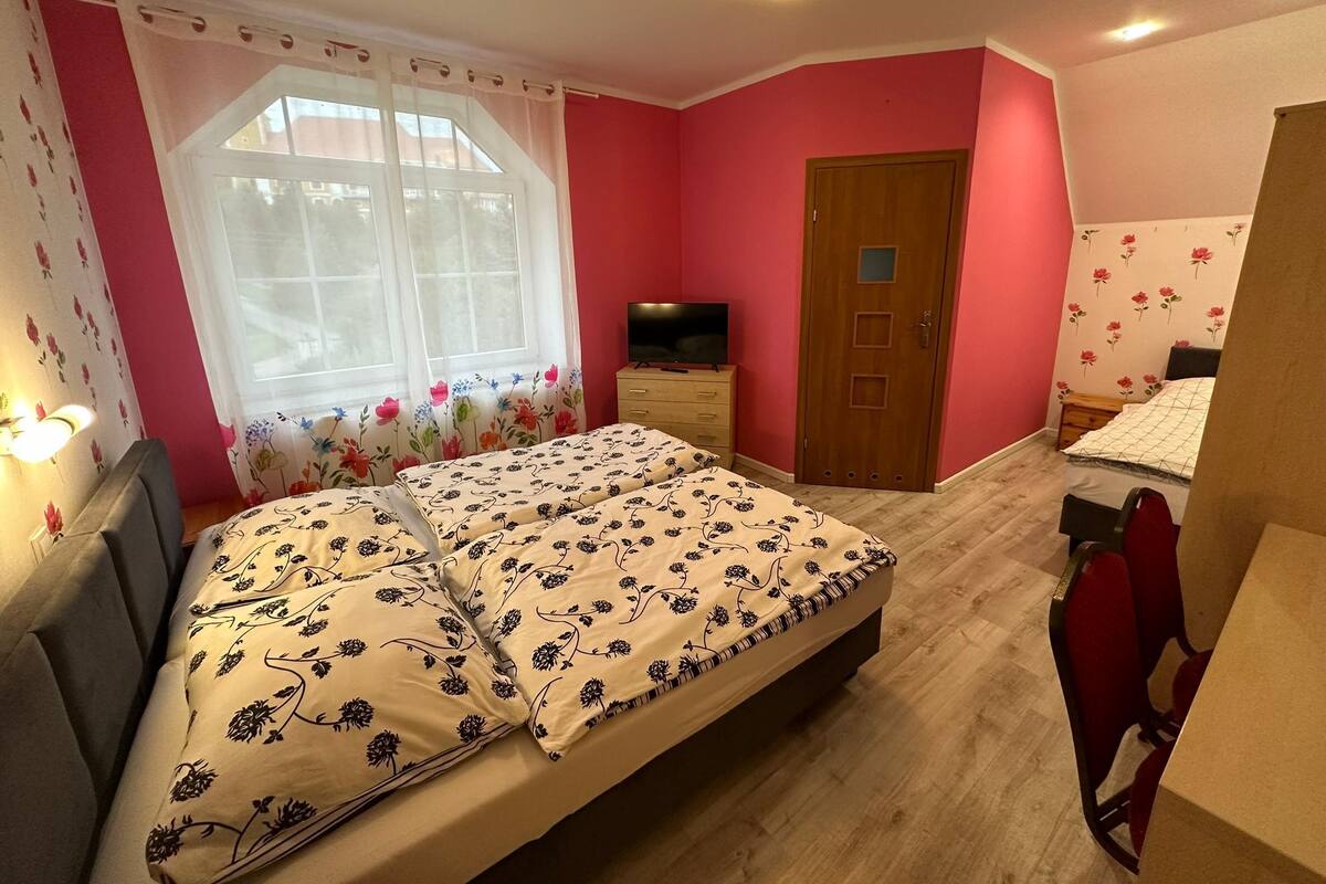 A bedroom with a bed, a television, a wooden door, and a window with floral curtains.
