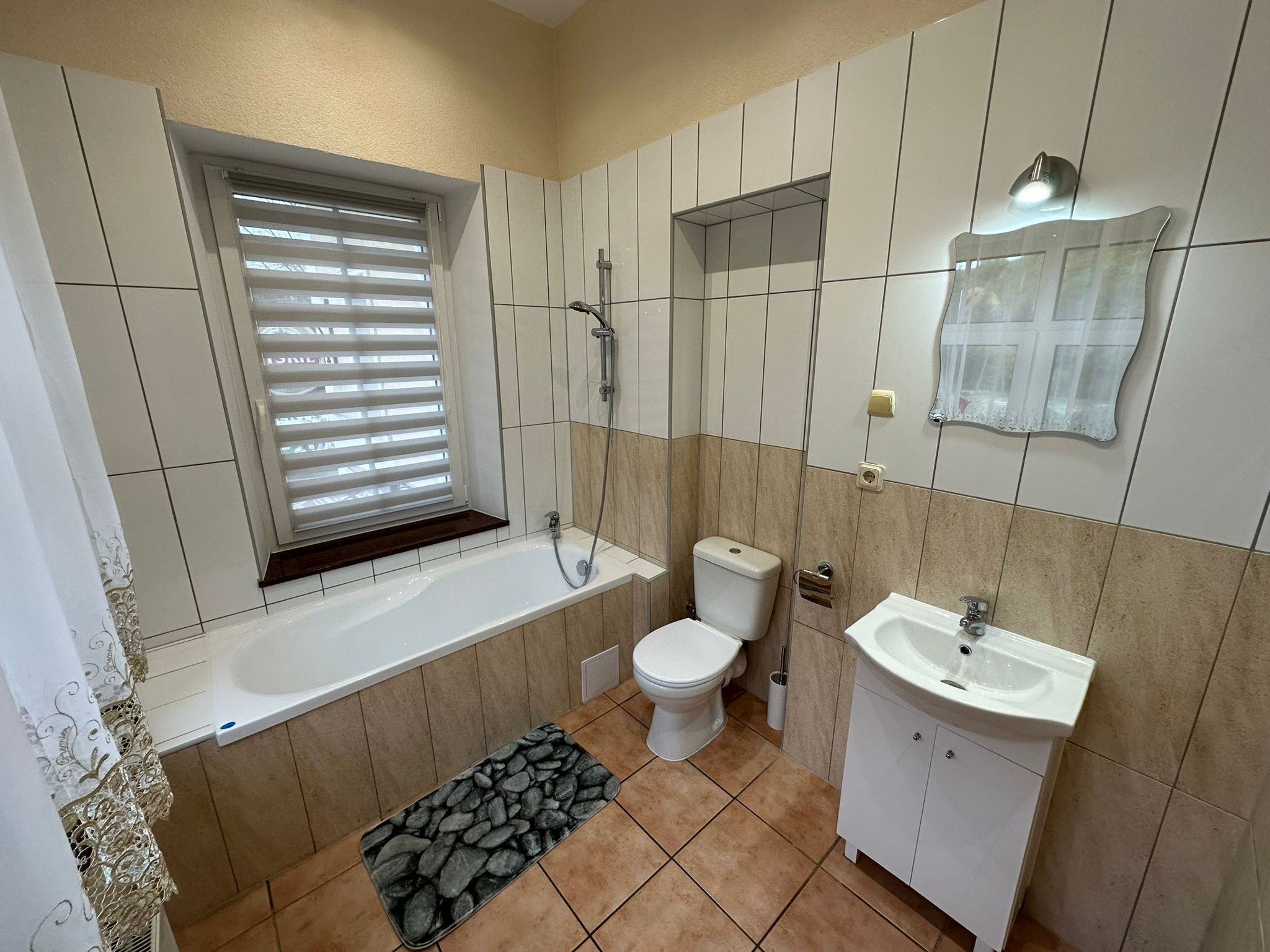 A bathroom with a bathtub, toilet, sink, and a window with blinds.