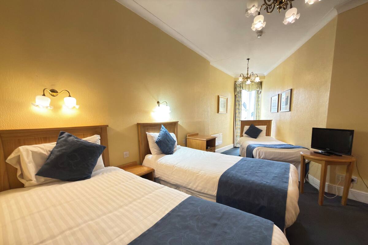 A hotel room with two beds, a television on a side table, and a chandelier.