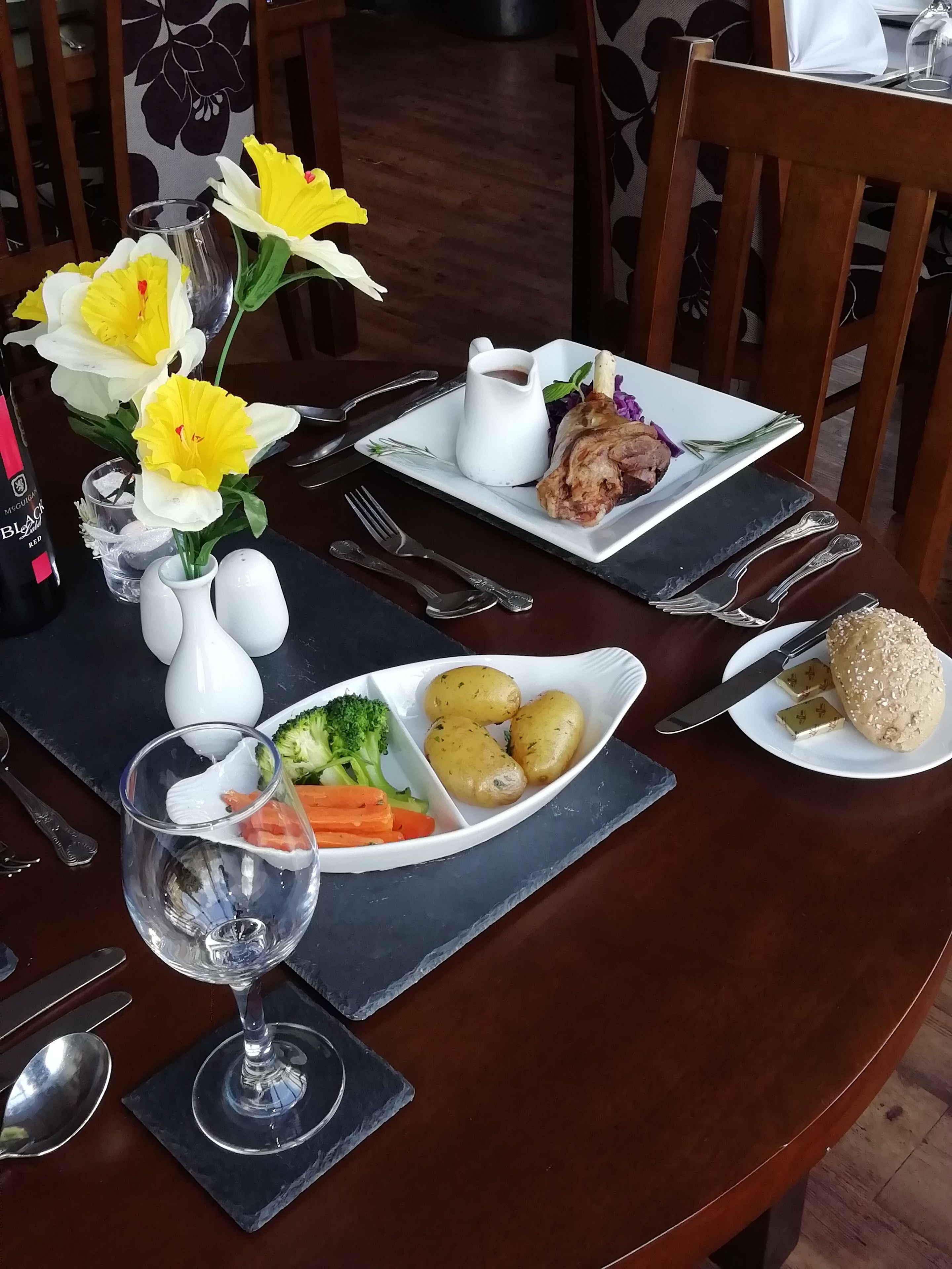 Une table à manger dressée avec des assiettes remplies de nourriture, un verre de vin et un vase de fleurs.