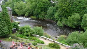 Une vue sur la rivière, avec un pont de pierre, des tables de pique-nique et une végétation luxuriante.