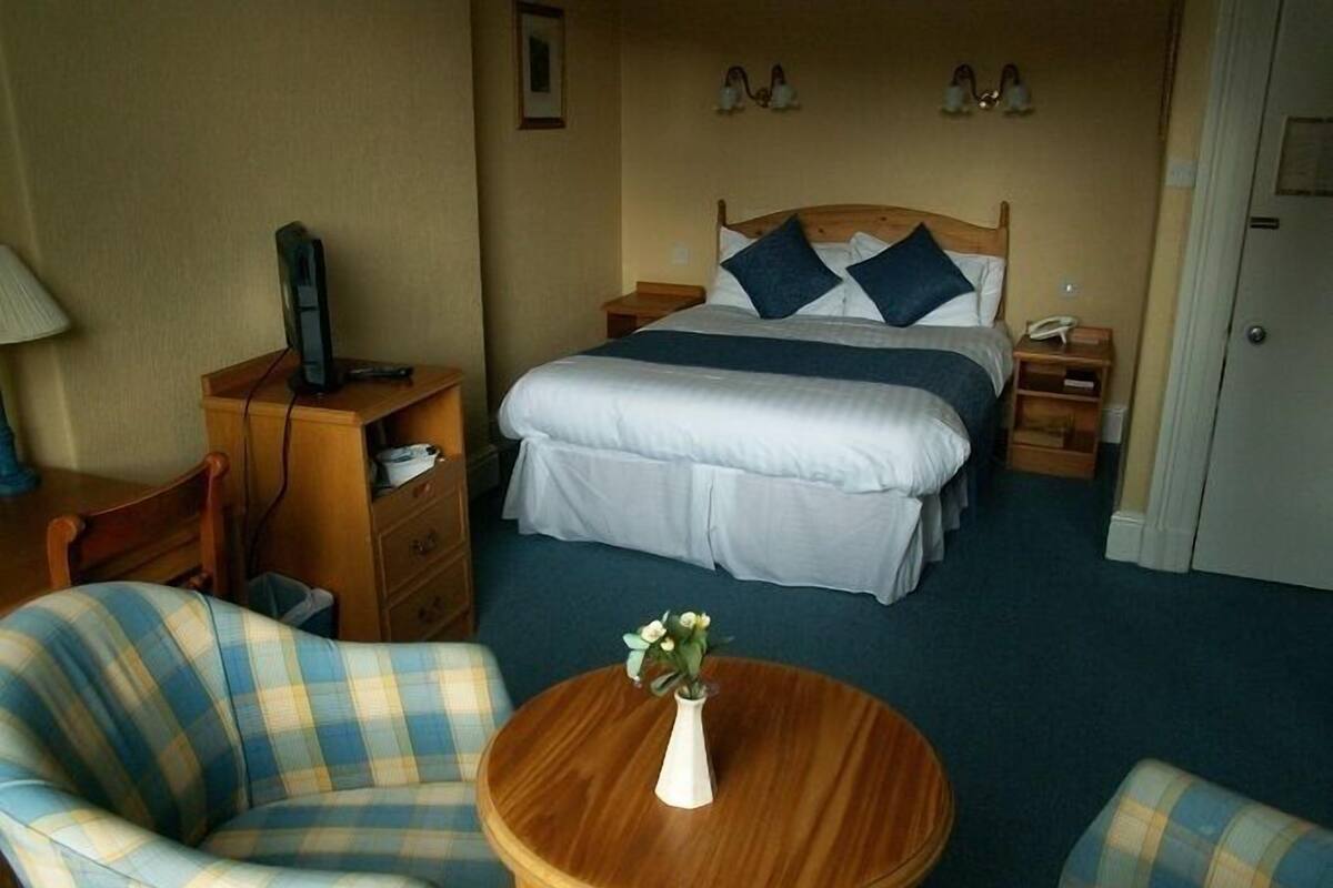A hotel room with a bed, two bedside tables, a desk, a chair, and a small table with a vase.