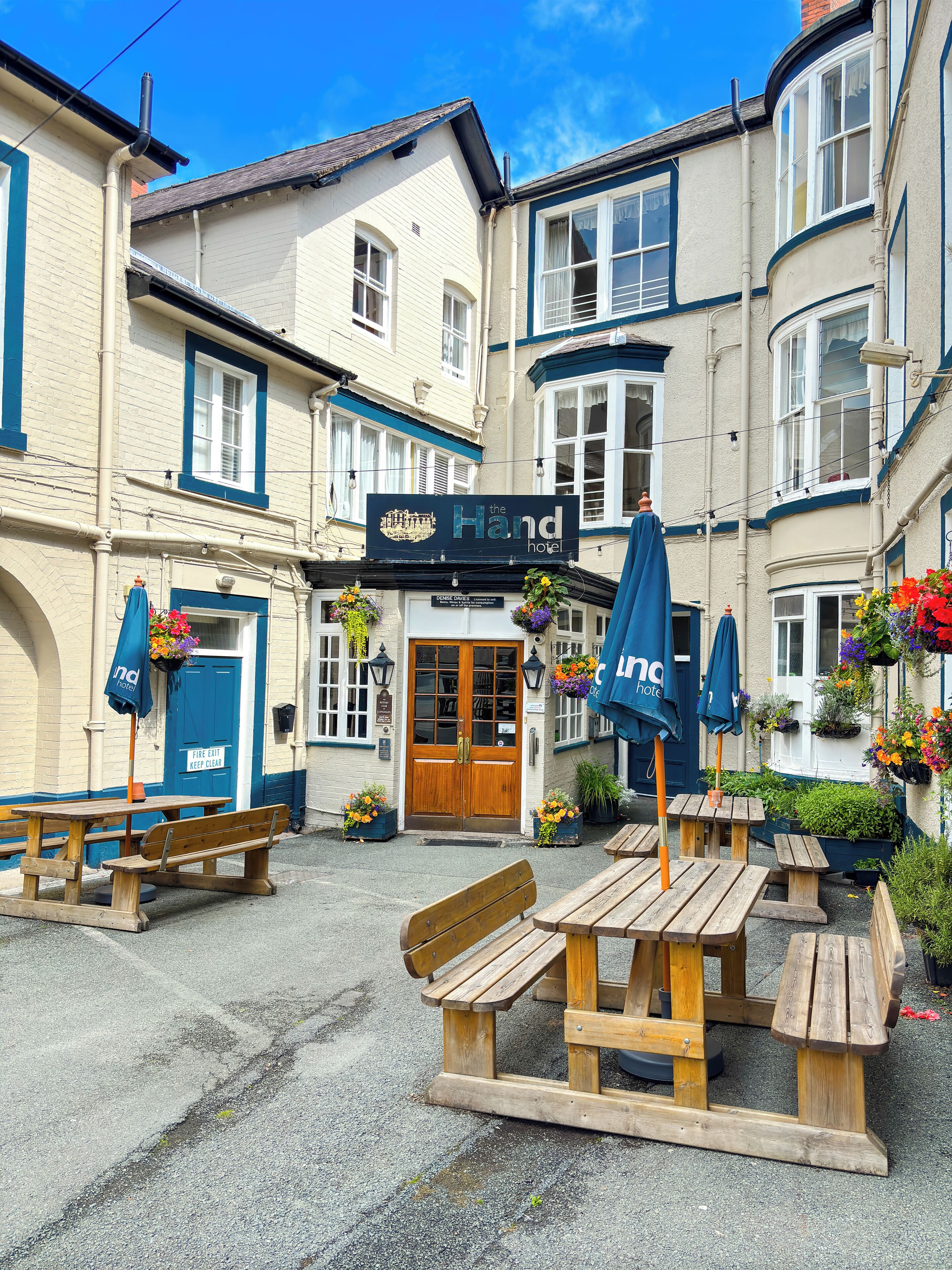 A hotel named 'The Hand' with a traditional facade, wooden benches, and flower baskets.