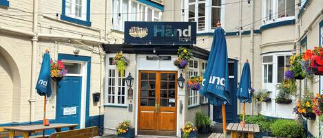 Een hotel genaamd 'The Hand' met een klassiek gevelontwerp, houten banken en bloemenmanden.
