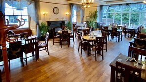 A spacious dining area with wooden tables and chairs, large windows, and a chandelier. - The Hand Hotel Llangollen by Compass Hospitality (Llangollen)