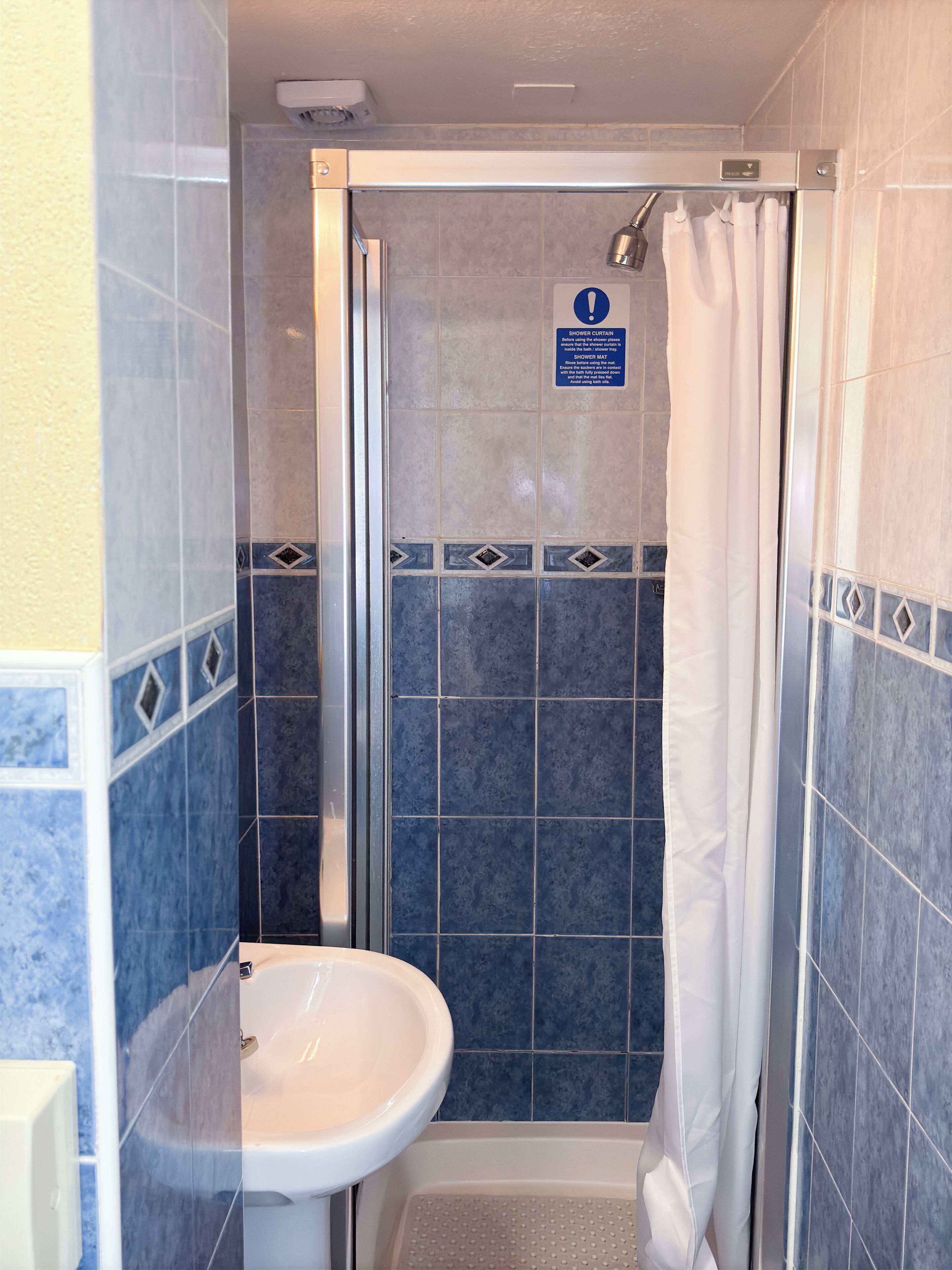 A bathroom with a shower, a sink, and a sign indicating the shower curtain should not be used.
