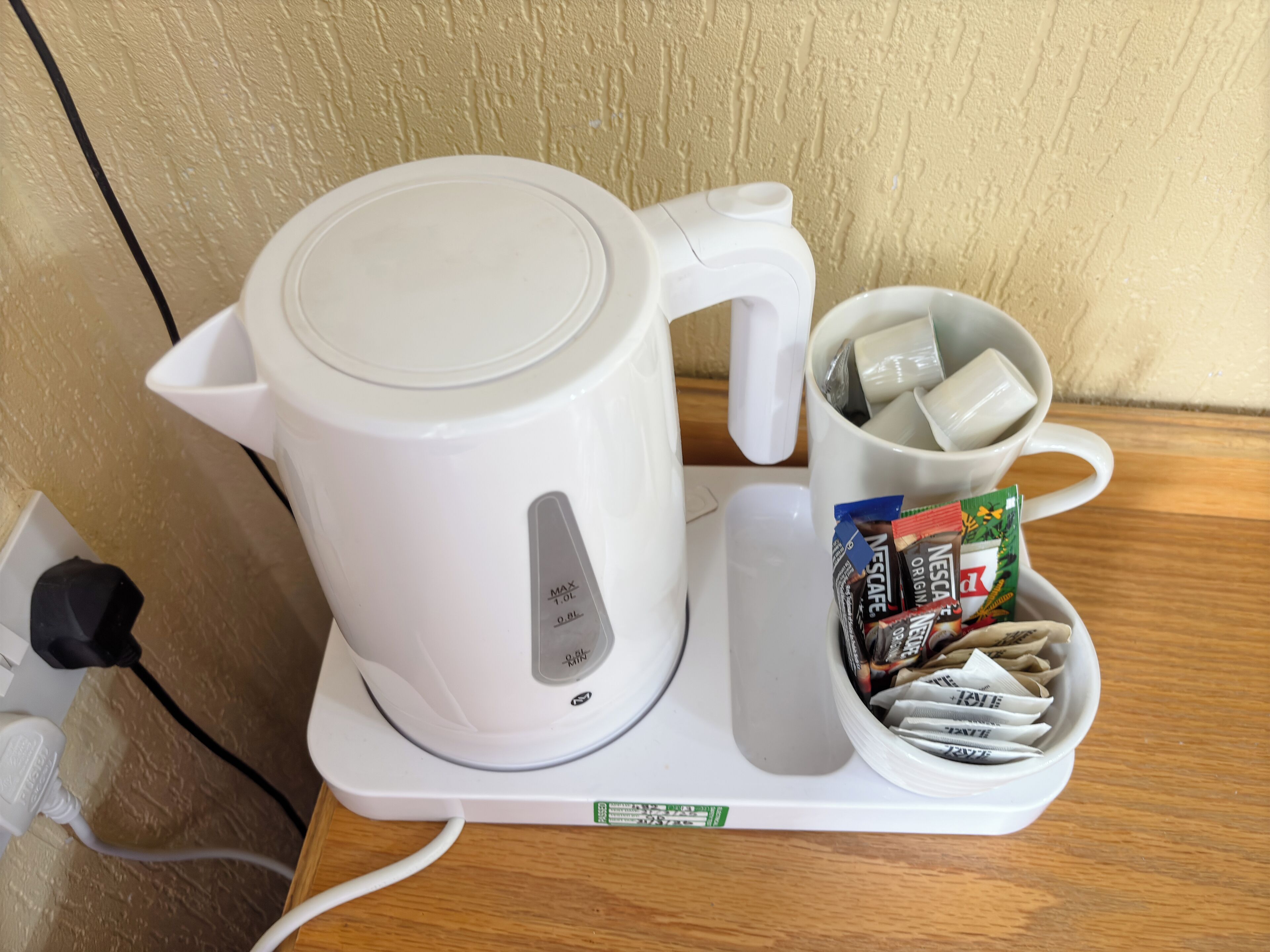 A white electric kettle on a white tray with a mug containing Nescafe capsules.