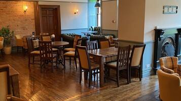 A spacious dining area with wooden flooring, multiple tables and chairs, a brick accent wall, and a fireplace.